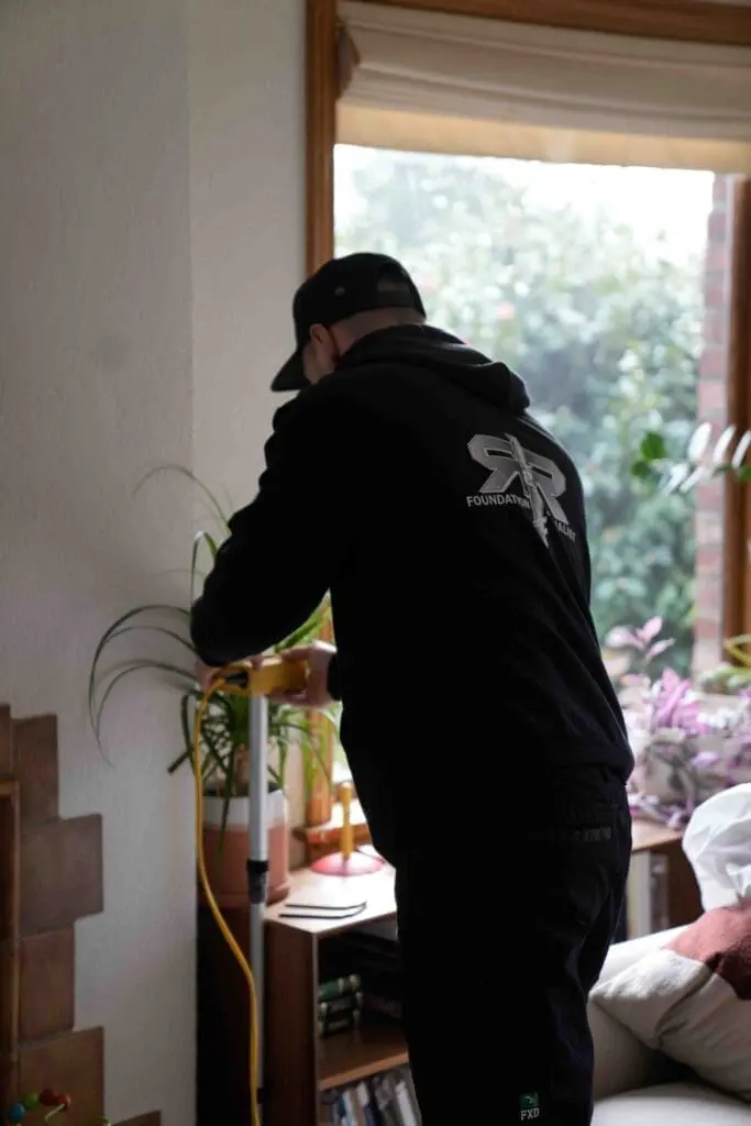 R&R male employee wearing a black sweatshirt measuring zip level against a wall in a home
